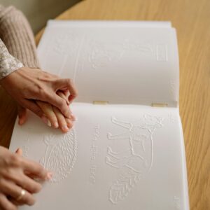 Close-up of hands reading a Braille book, depicting tactile learning for the visually impaired.