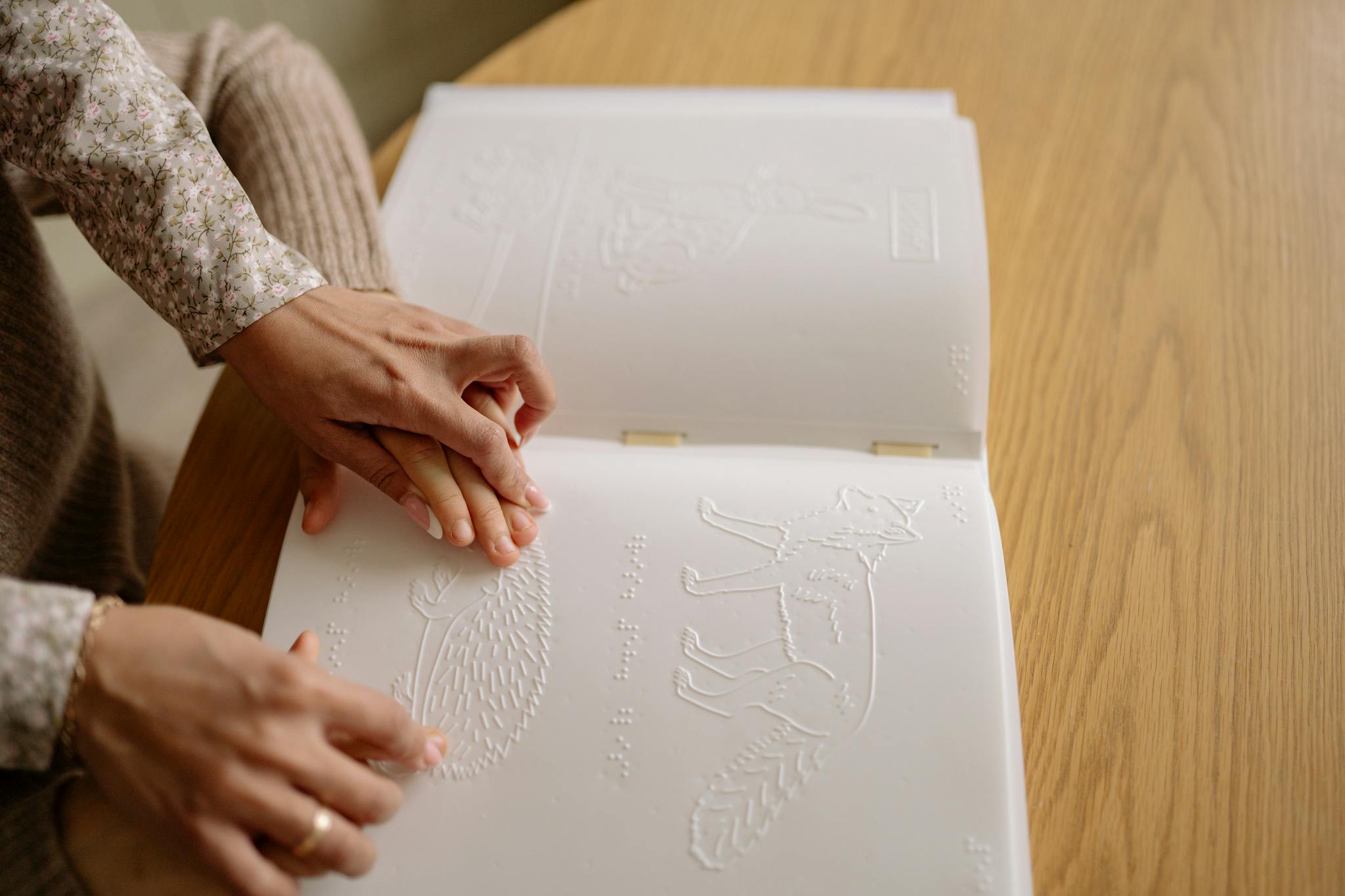 Close-up of hands reading a Braille book, depicting tactile learning for the visually impaired.