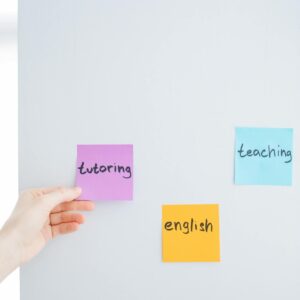 Hand placing sticky notes with words tutoring, teaching, and English on a wall, ideal for educational content.