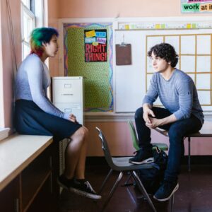 Two students engaged in a conversation in a classroom setting, reflecting an educational environment.